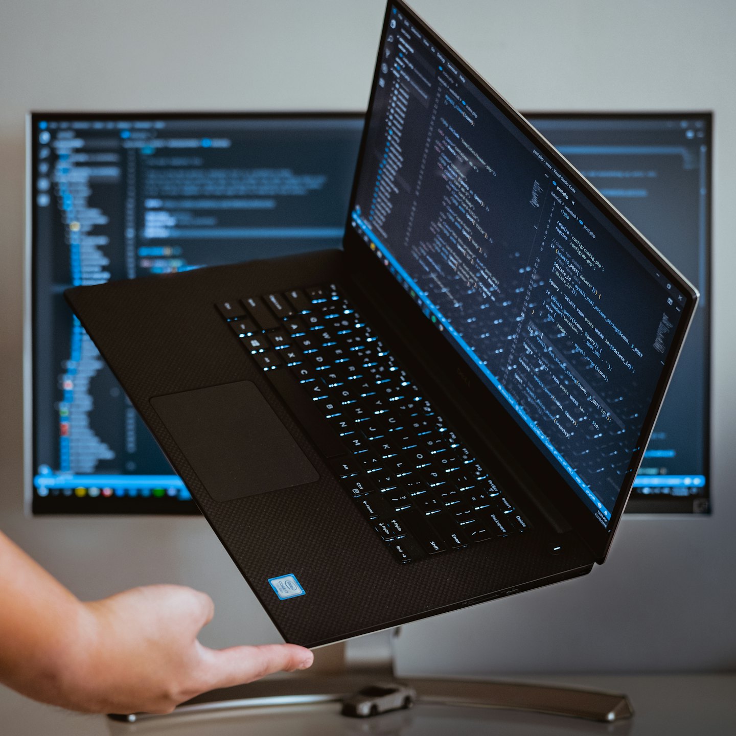 Hand holding open laptop with programming code.